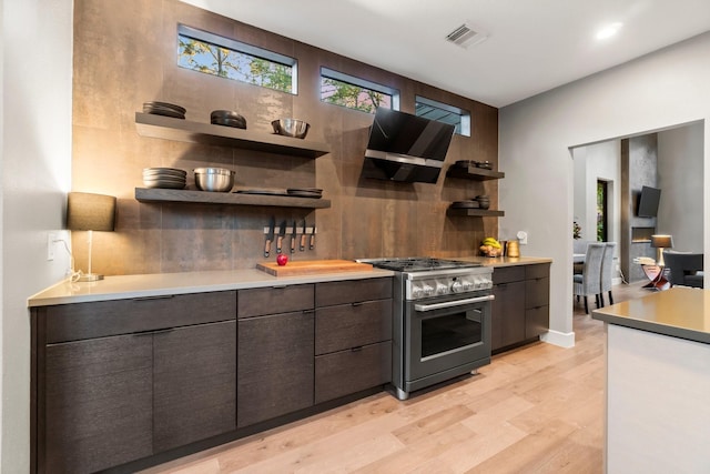 kitchen featuring high end stove, tasteful backsplash, light hardwood / wood-style floors, dark brown cabinets, and wall chimney exhaust hood