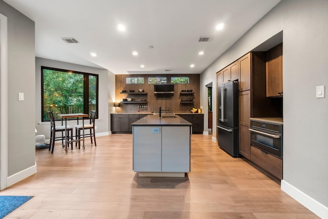 kitchen with sink, high end refrigerator, a center island with sink, black oven, and light hardwood / wood-style floors