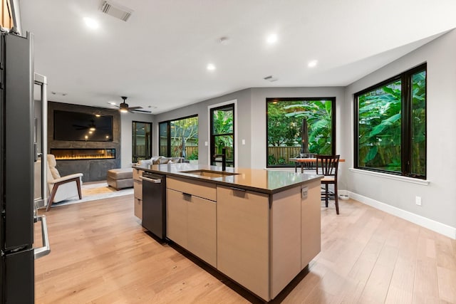 kitchen with a large fireplace, light hardwood / wood-style flooring, stainless steel refrigerator, and a center island with sink