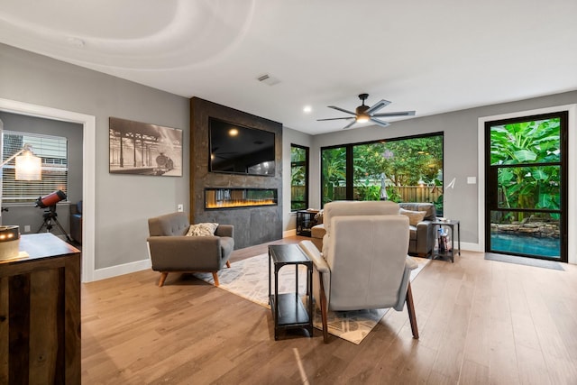 living room featuring ceiling fan, a large fireplace, and light hardwood / wood-style floors