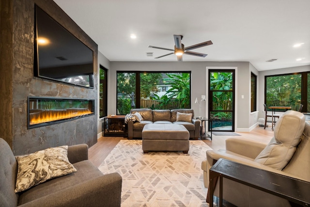 living room featuring a fireplace, ceiling fan, and light wood-type flooring