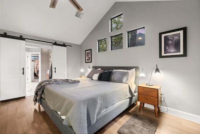 bedroom featuring hardwood / wood-style flooring, a barn door, high vaulted ceiling, and a walk in closet