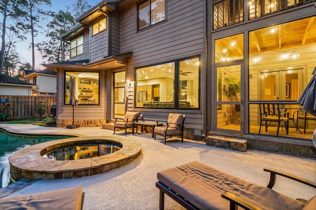 back house at dusk featuring a swimming pool with hot tub and a patio