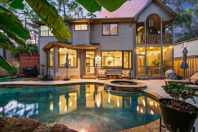 back house at dusk with a swimming pool with hot tub, a patio, and a balcony