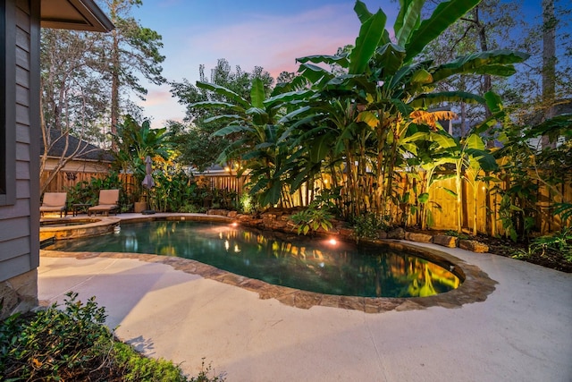 pool at dusk with a patio area and an in ground hot tub