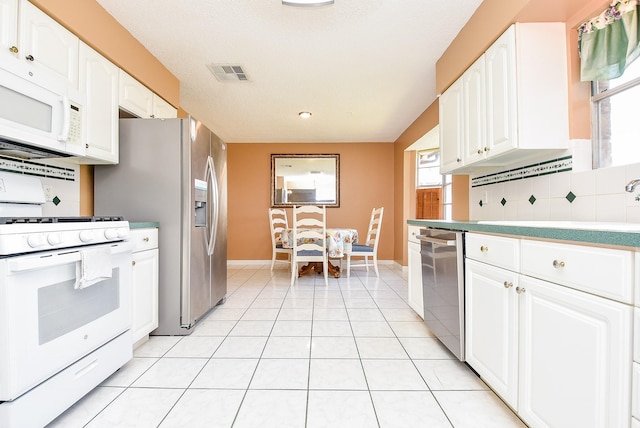 kitchen featuring visible vents, light tile patterned flooring, stainless steel appliances, decorative backsplash, and white cabinets