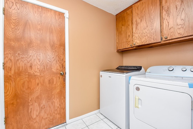 clothes washing area featuring light tile patterned floors, baseboards, cabinet space, a textured ceiling, and washer and dryer