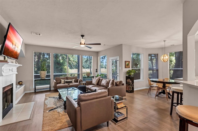 living room featuring light hardwood / wood-style flooring, ceiling fan with notable chandelier, and a fireplace