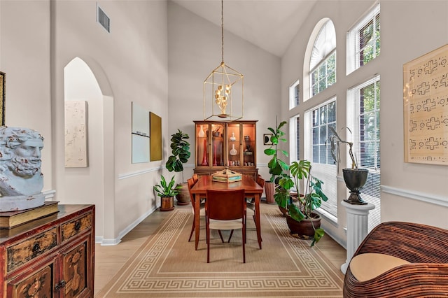 dining area with an inviting chandelier, high vaulted ceiling, and light hardwood / wood-style flooring