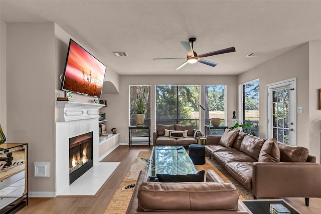 living room with a tiled fireplace, ceiling fan, and light wood-type flooring