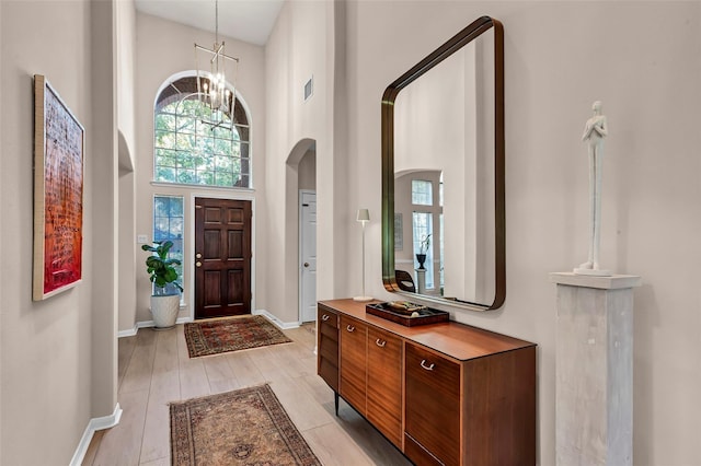 entryway with a towering ceiling, light hardwood / wood-style flooring, and a notable chandelier