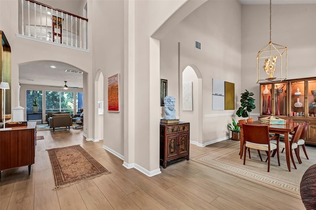 interior space featuring a towering ceiling, ceiling fan with notable chandelier, and light wood-type flooring