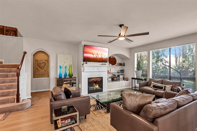 living room featuring a tiled fireplace, light hardwood / wood-style flooring, and ceiling fan