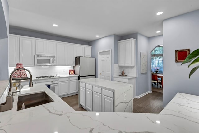 kitchen with stainless steel fridge, sink, white cabinets, and light stone counters