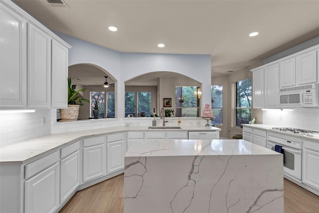 kitchen featuring sink, white appliances, a center island, light stone counters, and white cabinets