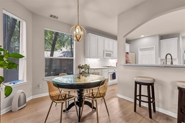 dining room with sink, an inviting chandelier, and light hardwood / wood-style floors