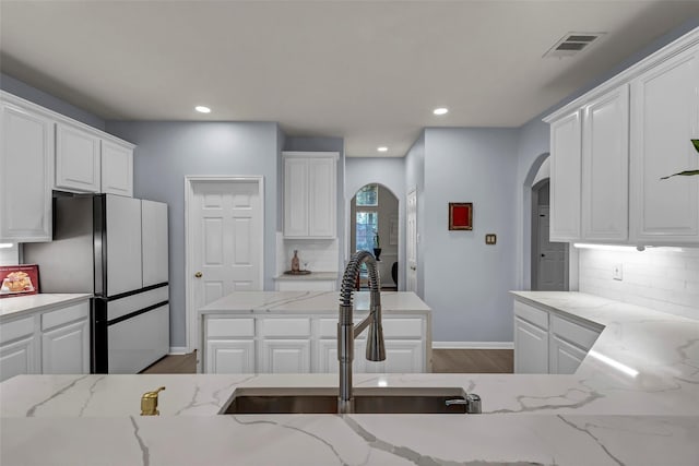 kitchen with white cabinetry, sink, light stone countertops, and stainless steel refrigerator