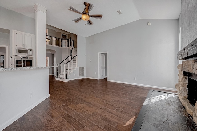 unfurnished living room with ceiling fan, high vaulted ceiling, dark hardwood / wood-style floors, a stone fireplace, and ornate columns