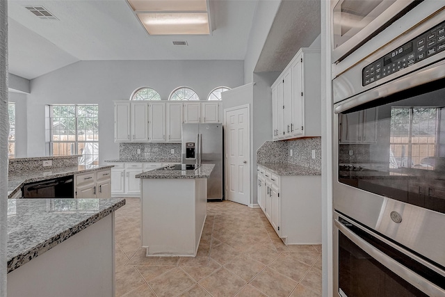 kitchen featuring light tile patterned flooring, light stone counters, black appliances, a kitchen island, and white cabinets