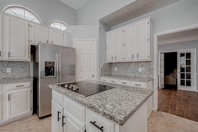 kitchen with stainless steel refrigerator with ice dispenser, a kitchen island, white cabinets, and black electric cooktop