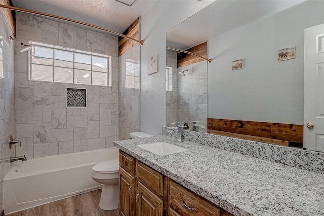 full bathroom with hardwood / wood-style flooring, vanity, tiled shower / bath combo, and toilet