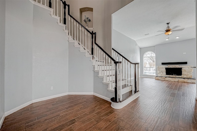 staircase featuring ceiling fan, wood-type flooring, a fireplace, and a towering ceiling