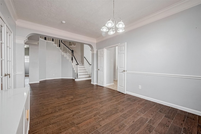 empty room featuring ornate columns, crown molding, a chandelier, a textured ceiling, and dark hardwood / wood-style flooring