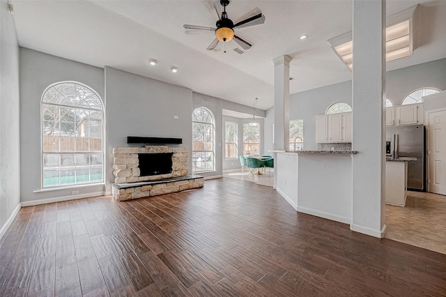 unfurnished living room with ceiling fan, dark hardwood / wood-style flooring, a stone fireplace, and ornate columns