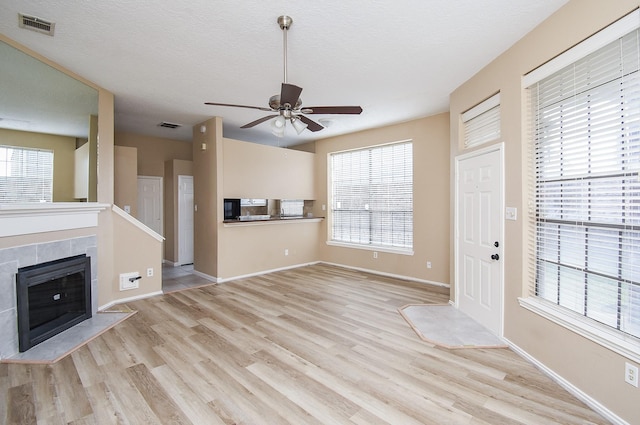 unfurnished living room with a tile fireplace, ceiling fan, a textured ceiling, and light wood-type flooring