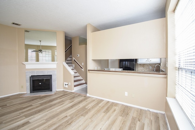 kitchen with sink, refrigerator, light hardwood / wood-style flooring, a textured ceiling, and a tile fireplace