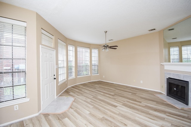 unfurnished living room featuring ceiling fan, a tiled fireplace, a textured ceiling, and light wood-type flooring