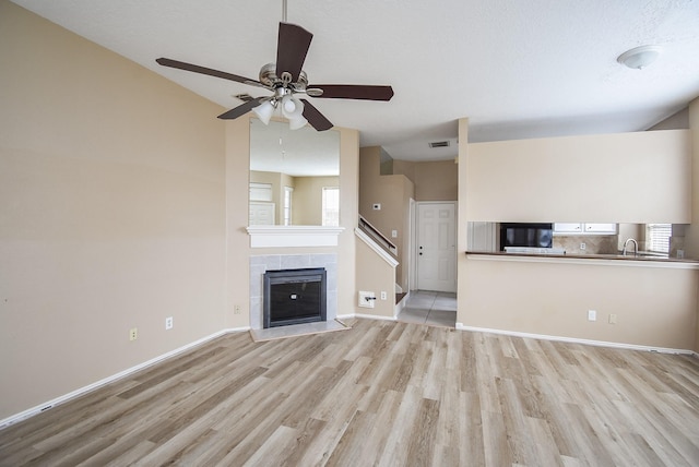 unfurnished living room featuring a tiled fireplace, sink, light hardwood / wood-style floors, and a healthy amount of sunlight