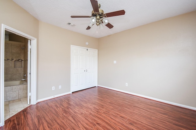 unfurnished bedroom with hardwood / wood-style floors, ceiling fan, a textured ceiling, ensuite bath, and a closet