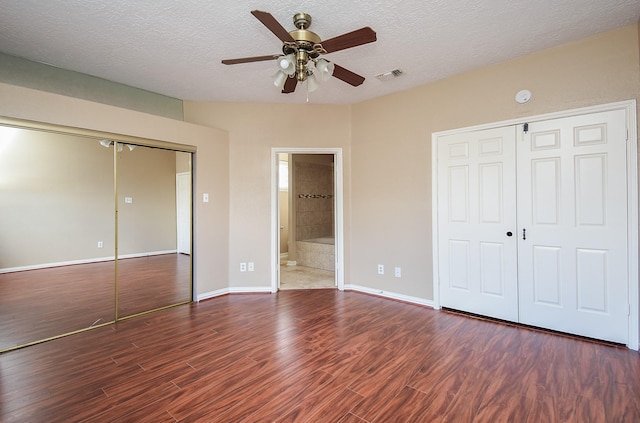 unfurnished bedroom featuring a closet, dark hardwood / wood-style floors, a textured ceiling, and ensuite bathroom