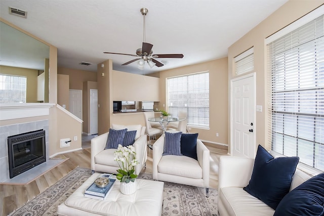 living room with a tiled fireplace, light hardwood / wood-style flooring, and ceiling fan