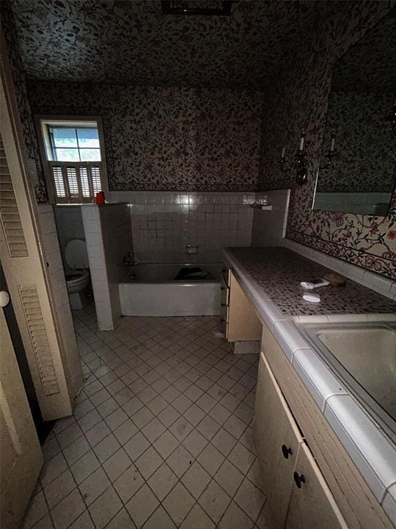 bathroom with tile walls, a tub to relax in, tile patterned flooring, vanity, and toilet