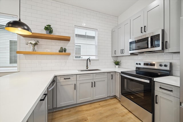 kitchen featuring stainless steel appliances, a sink, light countertops, open shelves, and pendant lighting