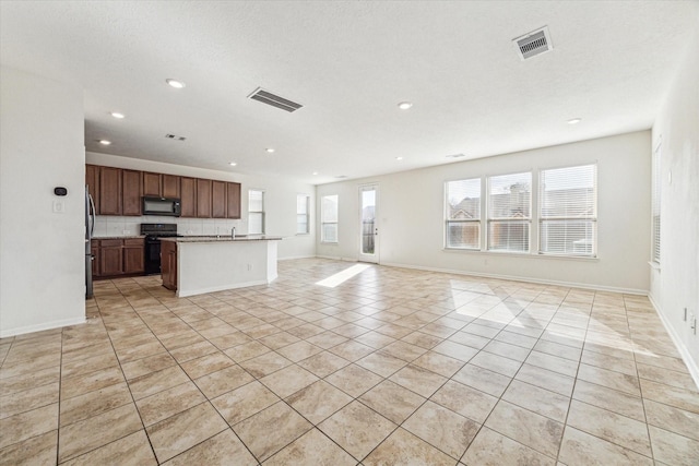 kitchen with stainless steel refrigerator, an island with sink, decorative backsplash, stove, and plenty of natural light