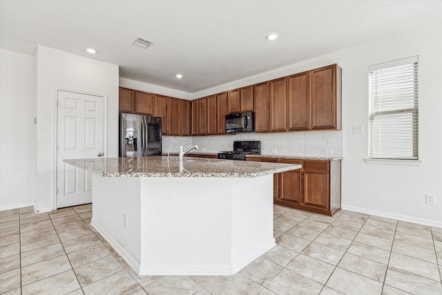 kitchen featuring an island with sink, sink, decorative backsplash, light tile patterned floors, and black appliances