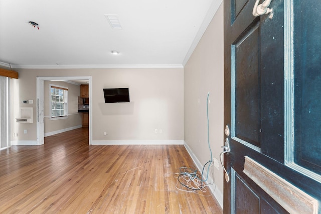 empty room with baseboards, crown molding, and light wood finished floors