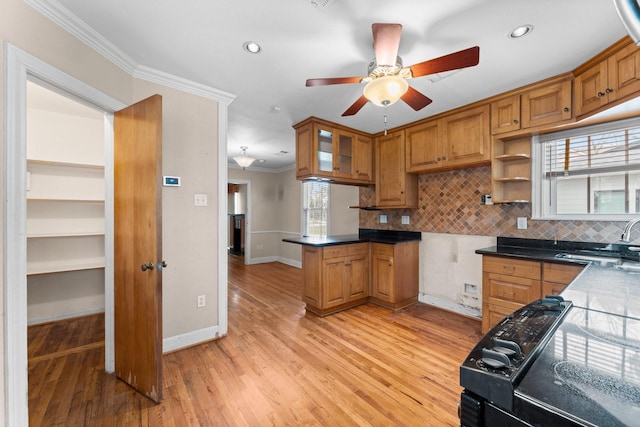 kitchen with a sink, ornamental molding, brown cabinets, dark countertops, and glass insert cabinets