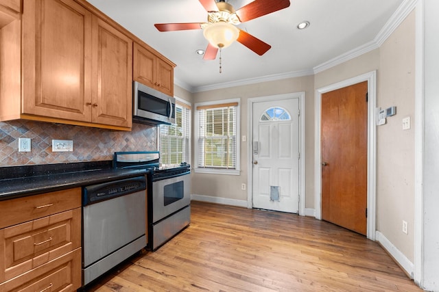 kitchen featuring crown molding, light wood finished floors, stainless steel appliances, dark countertops, and decorative backsplash