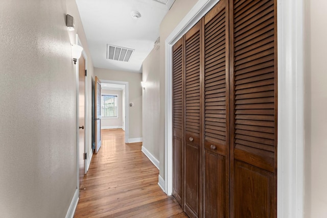 corridor featuring light wood finished floors, visible vents, and baseboards