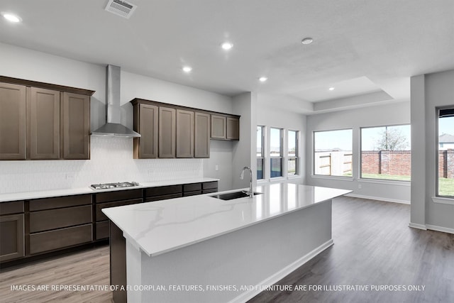 kitchen featuring visible vents, a sink, backsplash, light wood-style floors, and wall chimney range hood