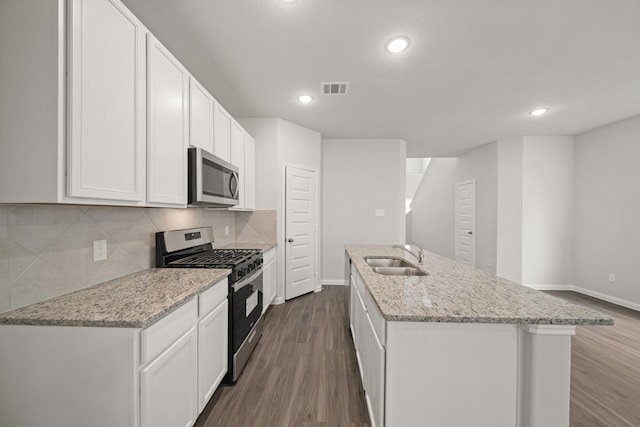 kitchen featuring a center island with sink, visible vents, stainless steel appliances, white cabinetry, and a sink