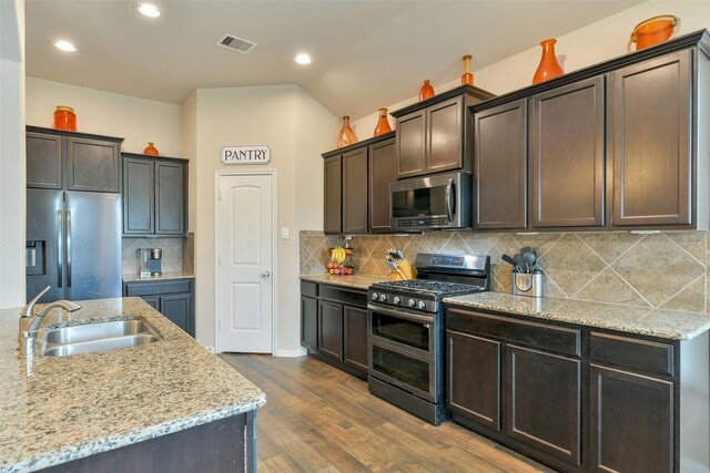 kitchen featuring sink, hardwood / wood-style floors, stainless steel appliances, dark brown cabinetry, and light stone countertops