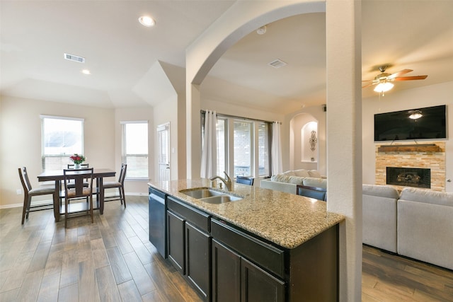 kitchen with sink, hardwood / wood-style flooring, dishwasher, a kitchen island with sink, and light stone counters