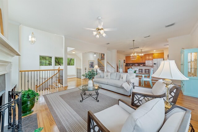 living room with a premium fireplace, crown molding, ceiling fan with notable chandelier, and light wood-type flooring