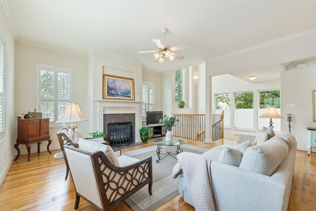 living room featuring a tiled fireplace, ornamental molding, and light hardwood / wood-style flooring