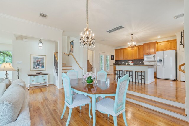 dining room with plenty of natural light, ornamental molding, light wood-type flooring, and a notable chandelier